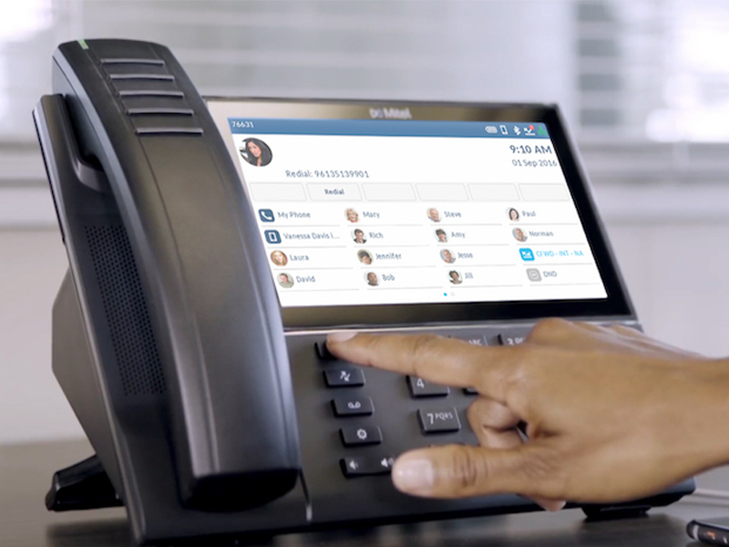 person dialing a contact number on deskphone