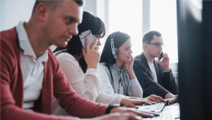 Office employees utilize a modern business phone system and headset-based office communication systems to manage customer calls and tasks in a collaborative work environment.