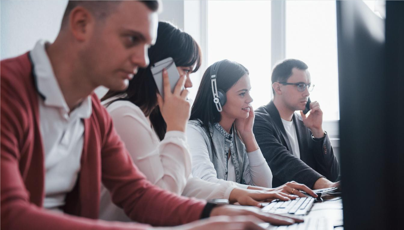 Office employees utilize a modern business phone system and headset-based office communication systems to manage customer calls and tasks in a collaborative work environment.
